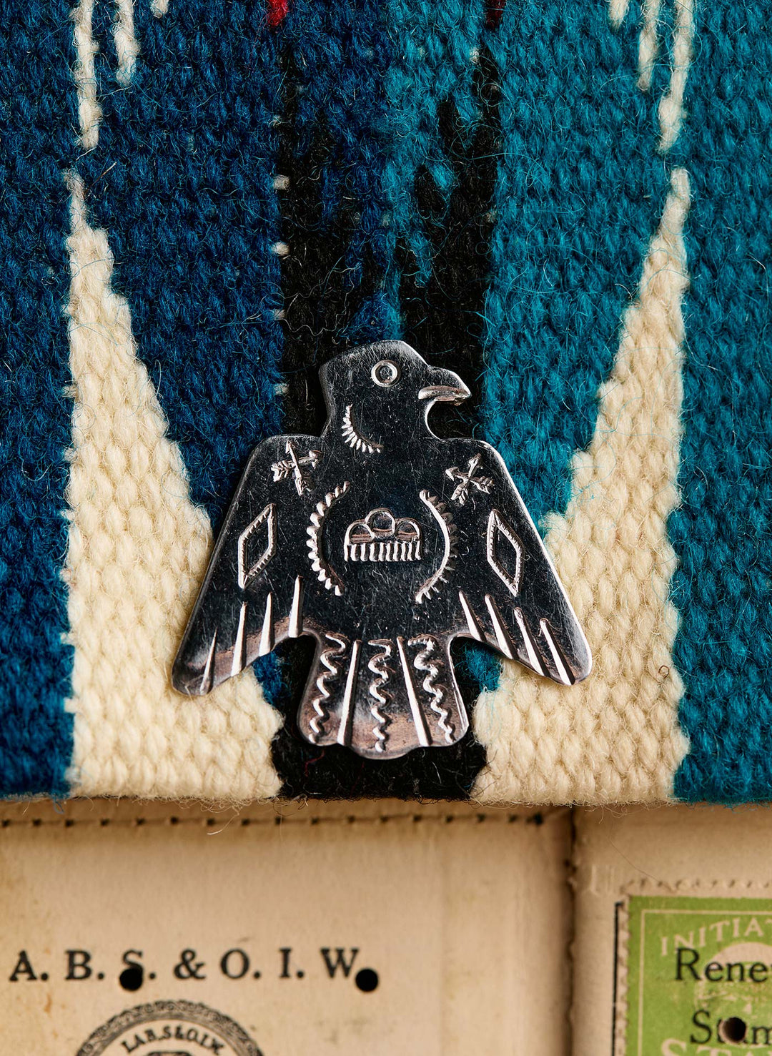 a metal bird pin on a blue and white striped fabric