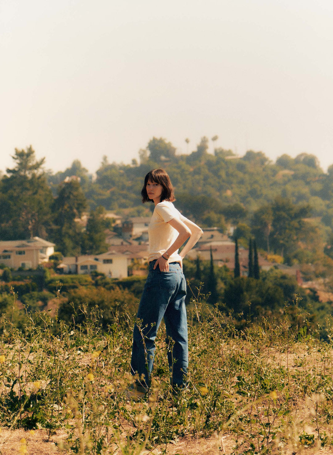 a woman standing in a field with houses in the background