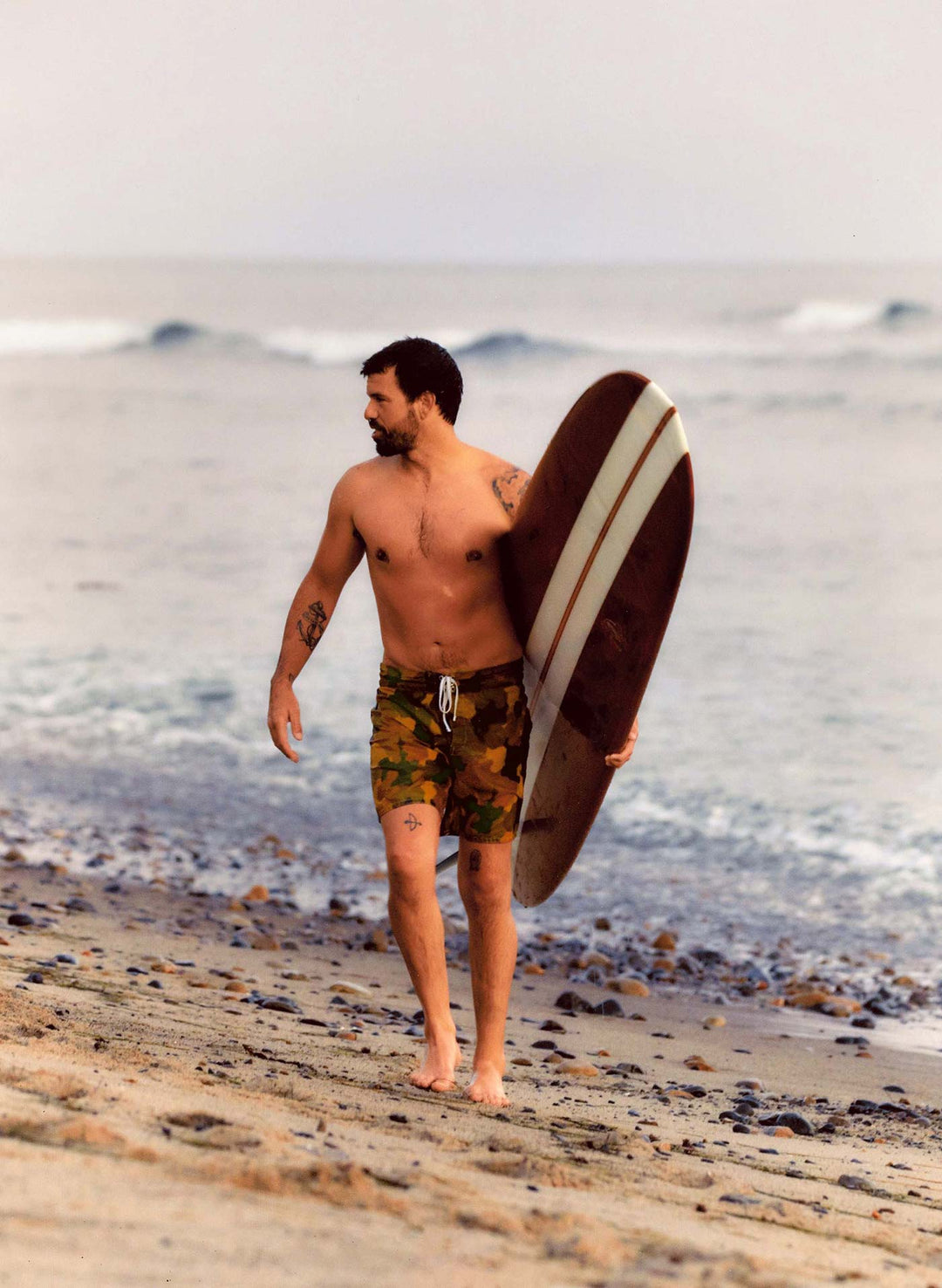 a man walking on a beach carrying a surfboard