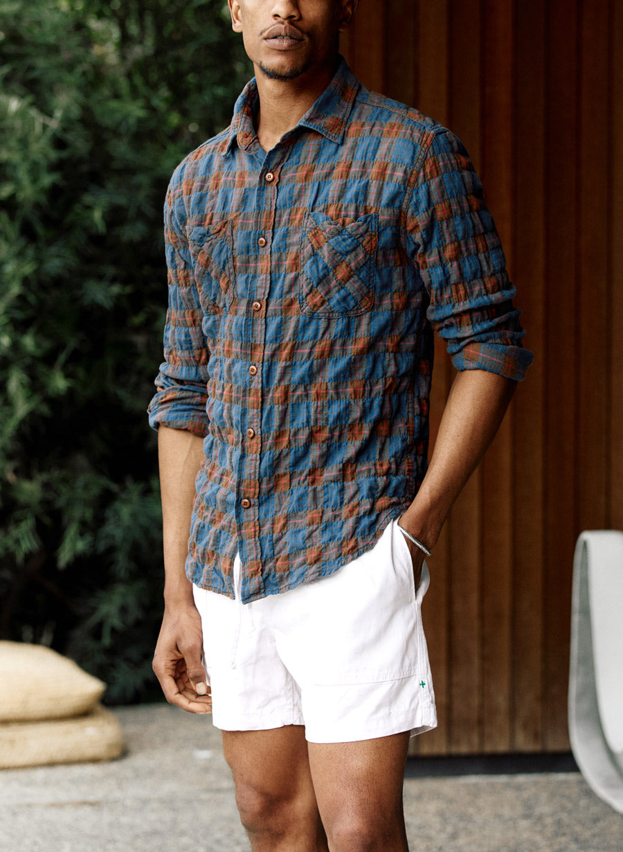 a man wearing a blue and brown plaid shirt and white shorts