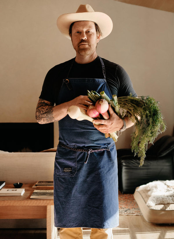 a man wearing a hat and apron holding vegetables