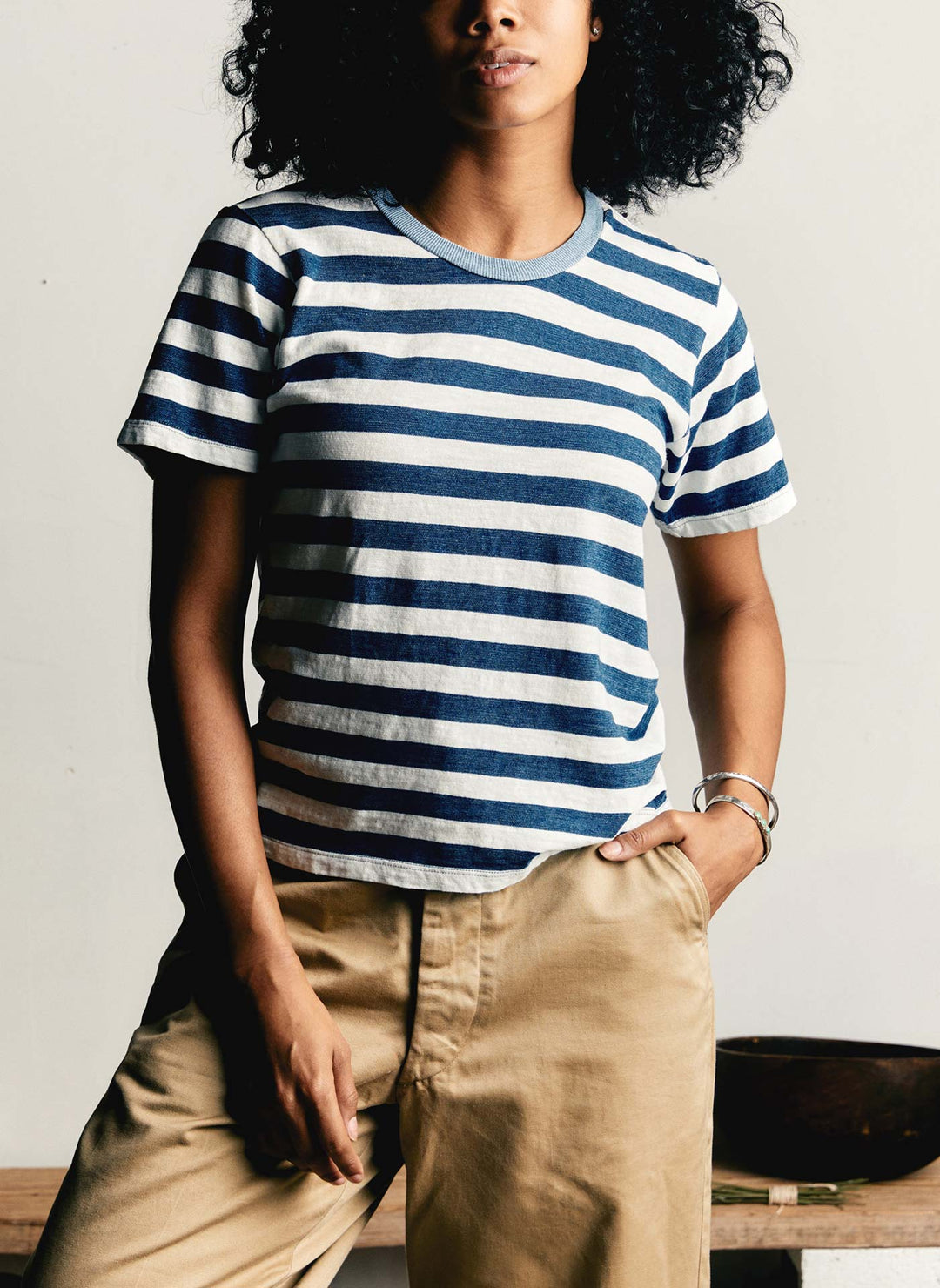 a woman with curly hair wearing a striped shirt and khaki pants