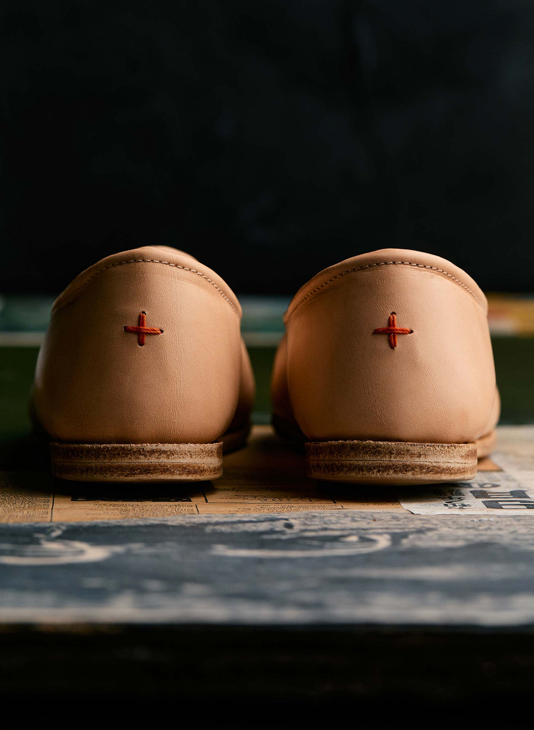 a pair of tan shoes with a red cross on the side