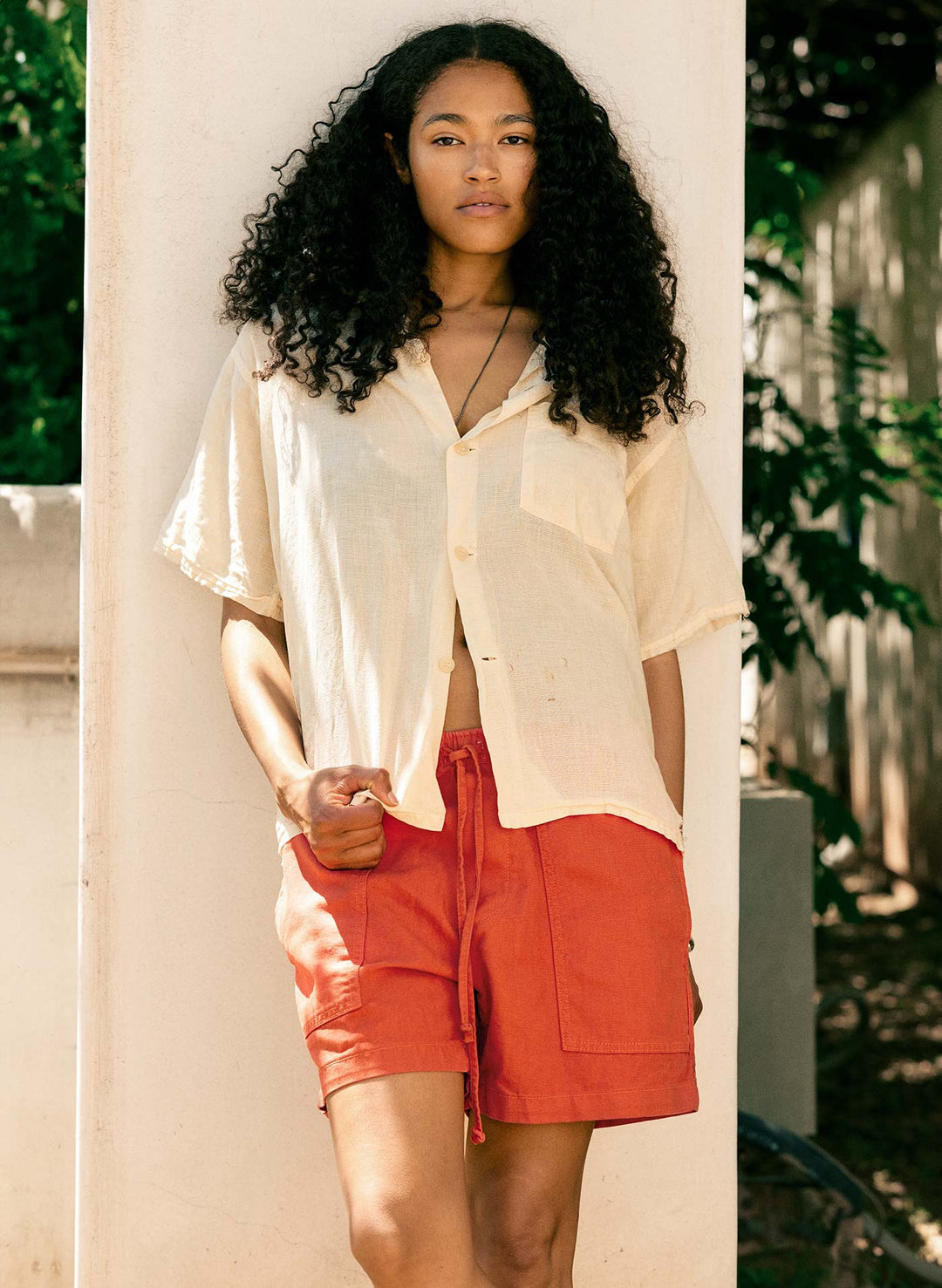 a woman with curly hair wearing a white shirt and red shorts