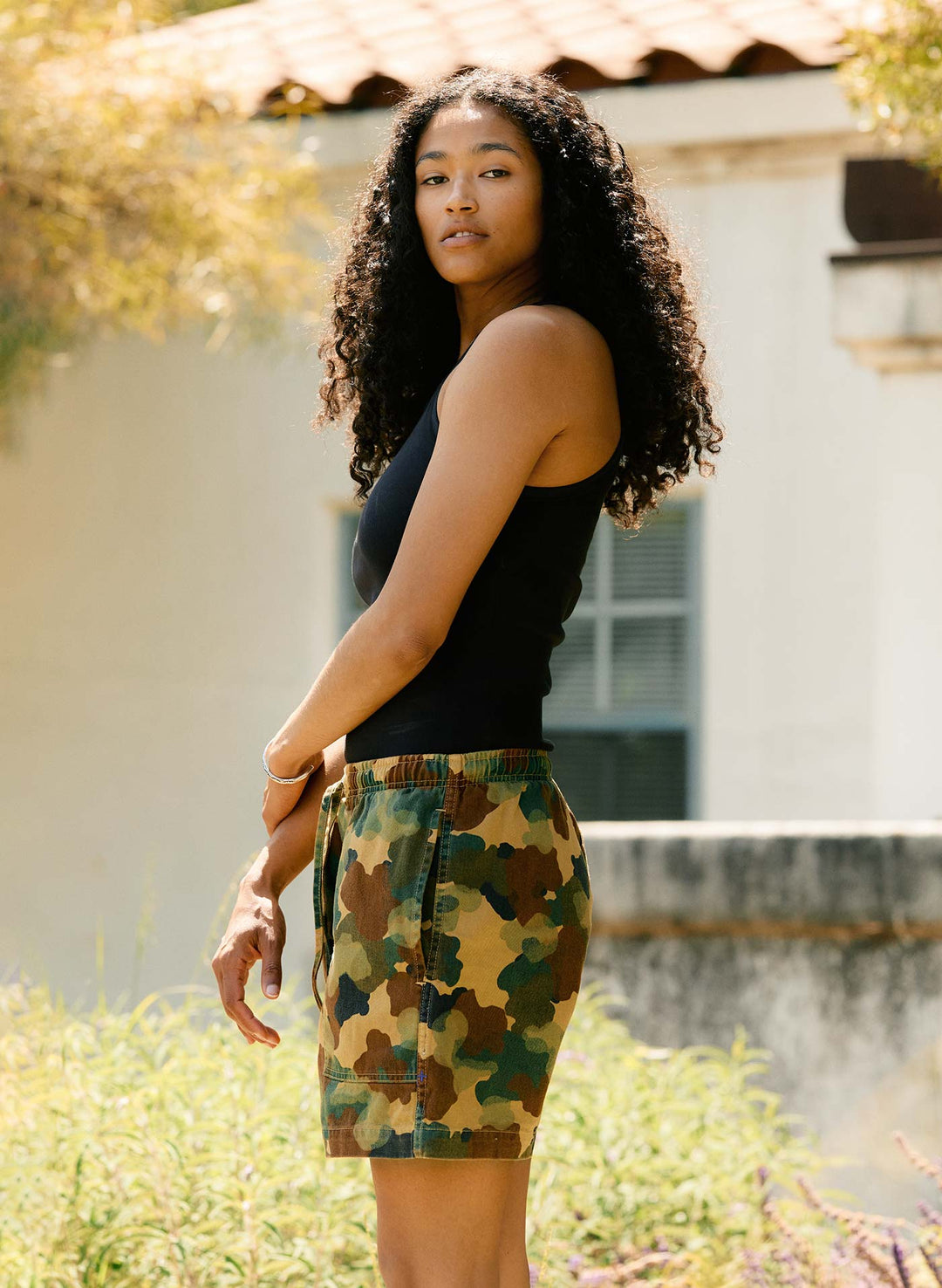 a woman with curly hair wearing camouflage pants