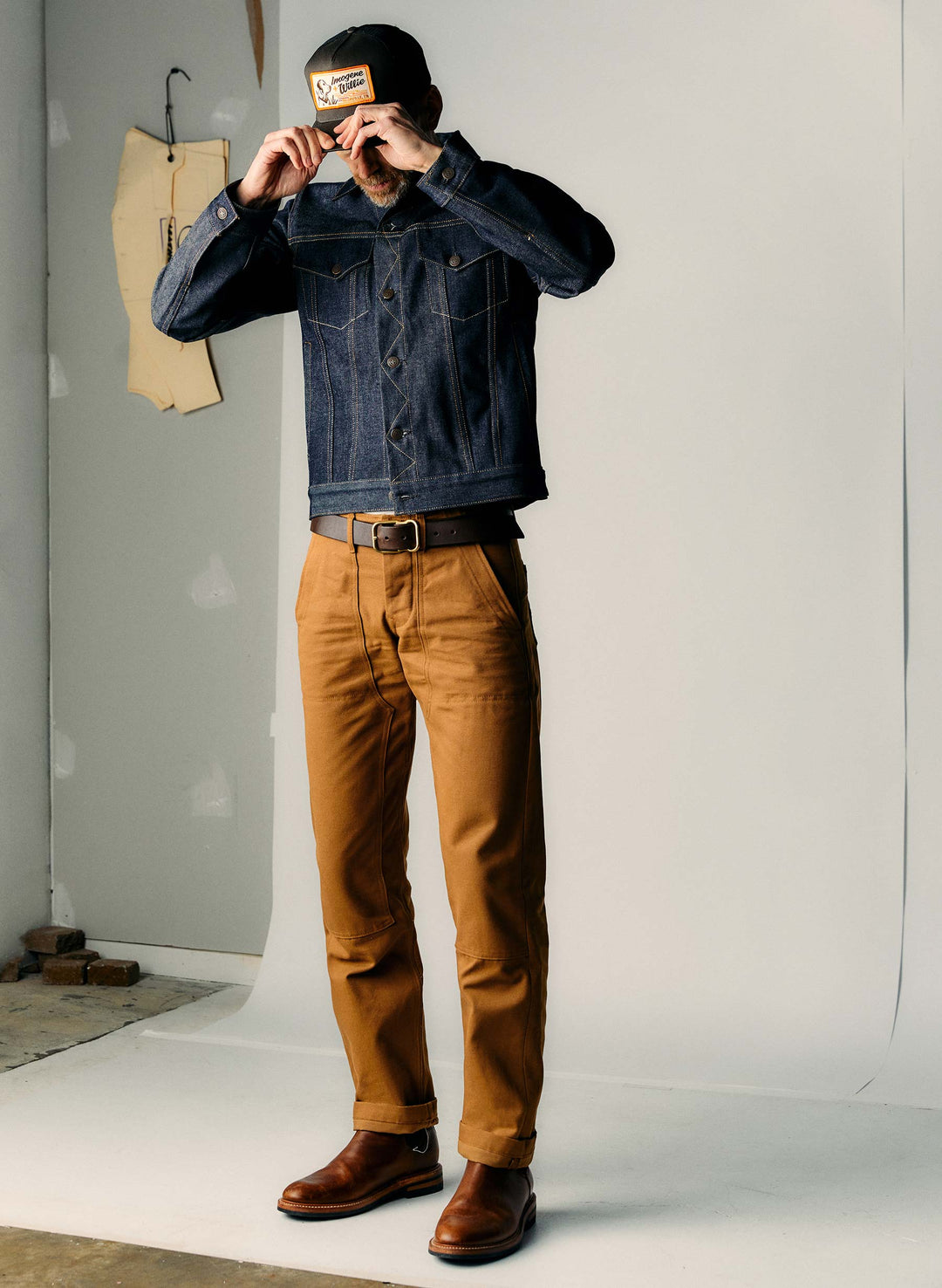 a man in a blue shirt and brown pants holding up his hat